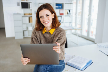 Wall Mural - young happy business woman sitting on a desk with laptop in her hands