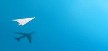 White Paper Plane Casting Shadow Of Airplane On Blue Background. Concept For Travel, Business Idea, Leadership, Success, Teamwork, Creative Idea, Vision.