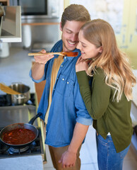 Wall Mural - Youve never tasted anything like it. Shot of an affectionate young couple tasting a sauce they are preparing together in their kitchen.