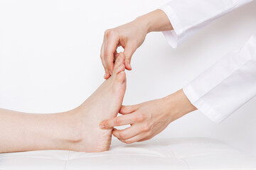 Examination of a young woman by an orthopedist. Cropped shot of female doctor holding a girl's foot in her hands on a white background. Flat feet, injury. Foot treatment. Pain from uncomfortable shoes