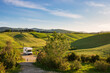 Camper van in unique green landscape, vanlife in Tuscany, Italy. Scenic dramatic sky and sunset light over cultivated hill range and cereal crop fields. Toscana, Italia.