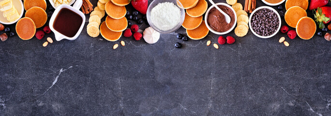Poster - Breakfast or brunch pancake buffet top border. Above view on a dark stone banner background. Mini pancakes with a selection of toppings.