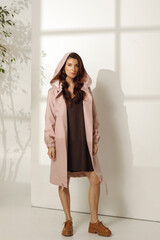 Female model wearing trendy spring outfit, pink raincoat against white background. Spring, summer fashion concept