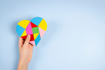 Wall Mural - Child hand holding colorful puzzle heart on light blue background. World autism awareness day concept