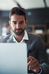 Fototapete - No work task is too tough for him to handle. Shot of a handsome young businessman using a laptop at his desk in a modern office.
