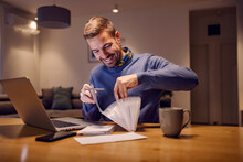 A Happy Man Sorting Bills And Paying Online From Home.