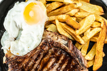 Plate with a juicy t-bone grilled or barbecued, accompanied by a portion of french fries and a fried egg. Traditional, homemade food concept.