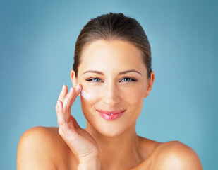 Canvas Print - Nourishment for my skin. Studio portrait of a beautiful young woman applying moisturizer to her face against a blue background.