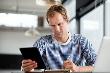 Poster - Modern day multitasking. Shot of a man working on a digital tablet and laptop in an office.