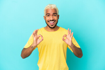 Poster - Young Colombian handsome man isolated on blue background showing ok sign with two hands