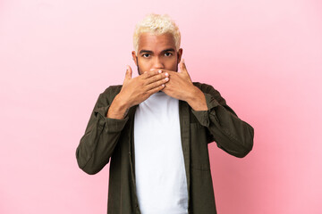 Wall Mural - Young Colombian handsome man isolated on pink background covering mouth with hands