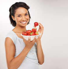 Wall Mural - Sweet, juicy and absolutely delicious. Portrait of a young woman enjoying a bowl of strawberries.