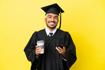 Sticker - Young university graduate Colombian man isolated on yellow background holding coffee to take away and a mobile