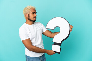 Wall Mural - Young Colombian handsome man isolated on blue background holding a question mark icon