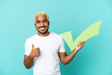 Poster - Young Colombian handsome man isolated on blue background holding a check icon with thumb up