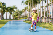 asian child or kid girl playing surf skate or skateboard in skating rink track and extreme sports to wearing helmet elbow pads wrist and knee support for body safety protect at bang phra public park