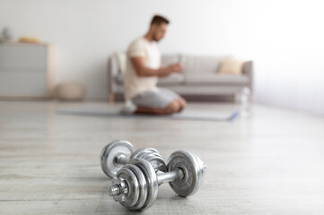 Wall Mural - Millennial Arab guy exercising at home during covid lockdown, selective focus on dumbbells