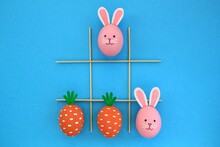 Creative Easter Theme Eggs With Carrot And Bunnies On Blue Background. Kids Playing Tic-tac-toe At Egg Hunt Concept. Creative Game Idea For Family, Minimal Lay Out For Banner, Magazine, Poster, Web