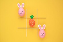 Creative Easter Theme Eggs With Carrot And Bunnies On Yellow Background. Kids Playing Tic-tac-toe At Egg Hunt Concept. Creative Game Idea For Family, Minimal Lay Out For Banner, Magazine, Poster, Web