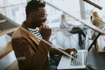 Young African American business man working on laptop computer while sitting on a office stairs