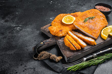 Fried Sliced Weiner Schnitzel On A Wooden Board With Herbs. Black Background. Top View. Copy Space