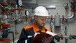 © ShantiMedia - An engineer at a pumping station records pressure and temperature readings. Work in the oil and gas industry. A man in a white helmet with a beard at the workplace in the factory.