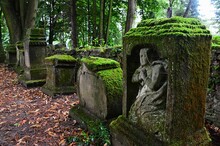 Ancient Moss Covered Remains Of Cemetery Gravestones, One In Front With Scuplture Of Praying Person, Located On Church Cemetery In Orava Region, Northern Slovakia. Humid Cloudy Day