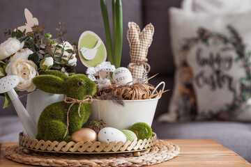 Wall Mural - Rustic. White-green colors. Iron planters with Easter eggs, flowers, candles and rabbits in the living room interior on the table. The concept of home comfort in the bright holiday of Easter 2022.