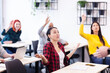 © Nikola Spasenoski - Multi ethnic students listening to a lecturer in a classroom. Smart young people rasing hands during class.