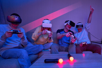 Wall Mural - friends playing virtual reality games using joysticks while sitting on the couch.