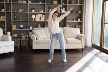 Happy carefree Hispanic girl dancing to music in living room, listening to radio, songs, moving body, laughing, enjoying energetic activity, exercises. Cheerful dancer woman having fun at home