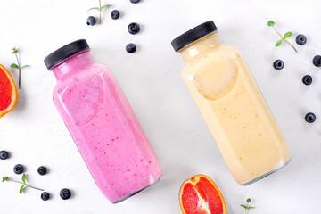 Smoothies with berries and fruits in two glass bottles on the white table. Healthy drink variation and kids food. Flat lay