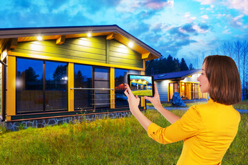 Wall Mural - Woman takes pictures of the cottage on an electronic tablet. Girl in a cottage village. Sale of wooden houses. A female realtor. Rental of cottages. Wooden houses on the background of nature.