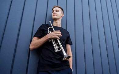 Young street musician playing the trumpet near the big blue wall