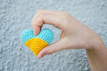 Yellow And Blue Heart Crochet In Children's Palms On A Blurred Natural Background.