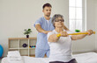 Training and recovery with rehabilitation specialist. Senior woman with elastic tape doing stretching exercise with male physiotherapist. Doctor helps woman sitting on bed with her arms outstretched.