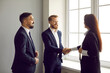 © Studio Romantic - Business partnership.Happy business people shake hands in agreement and end successful meeting in office.Two men and woman in business attire rejoice in partnership and shake hands standing by window