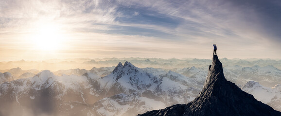 adventurous man hiker standing on top of icy peak with rocky mountains in background. adventure comp