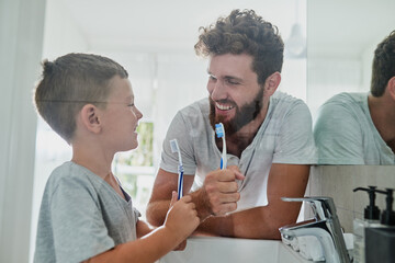 Got to take care of our teeth. Shot of a father and his little son brushing their teeth together in the bathroom at home.