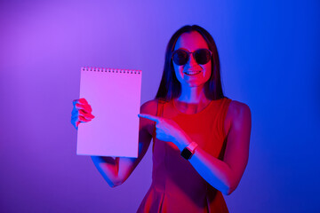 happy girl showing blank paper notebook in neon lights