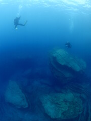  scuba divers around a reef underwater deep blue water big rocks  air bubbles rising