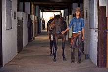 Heading Out To Catch An Outlaw. Shot Of A Cowgirl Leading A Horse Out Of A Stable.