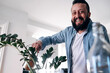 © Westend61 - Happy man watering plant at home