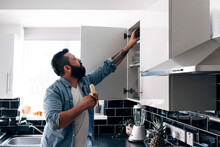 Man With Banana Searching In Cabinet At Kitchen