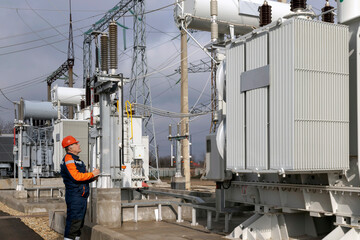 An electrical engineer inspects power transformers in power plants. An engineer in a red helmet and protective overalls. Substation work