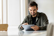 © Westend61 - Smiling man sitting at table using tablet PC at home