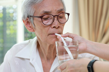 Wall Mural - Nurse or caregiver taking care of disabled senior grandmother gives drinking water,feeding water using a straw to prevent choking and  difficulty or discomfort in swallowing,dysphagia in the elderly