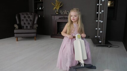 pretty little girl in purple dress with long blond hair rides toy horse in dark room, 4k