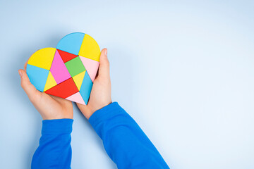 Wall Mural - Child hands holding colorful puzzle heart on light blue background. World autism awareness day concept