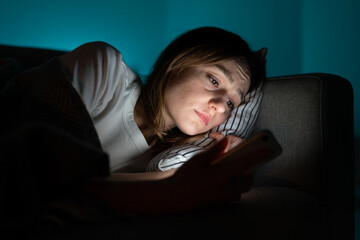 Wall Mural - Unhappy woman lying in bed with smartphone, following ex-boyfriend on social media, sad female using mobile phone at night, can not sleep after relationship breakup, suffering from insomnia. Anxiety.